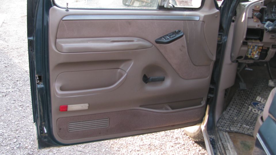 1992 Ford Bronco interior door panel with brown fabric and plastic trim, showing window controls and door handle