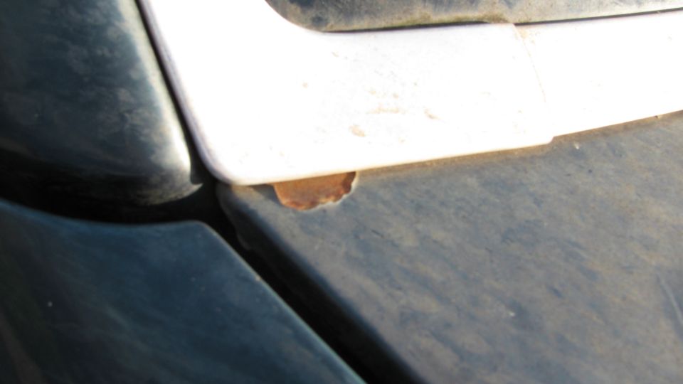 Close-up of rust spot on dark body panel edge beneath white trim piece