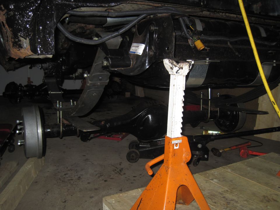 Undercarriage of a vehicle on jack stands, showing suspension and rear axle components