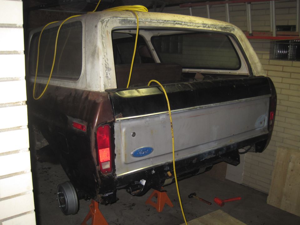 Rear view of a 1979 Ford Bronco with a brown lower body and black upper body, on jack stands