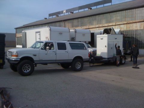 1996 Ford C-350 (Centurion Conversions) - A white 1996 Ford C-350 Centurion Conversions SUV is seen from the side, towing a trailer with a portable building.