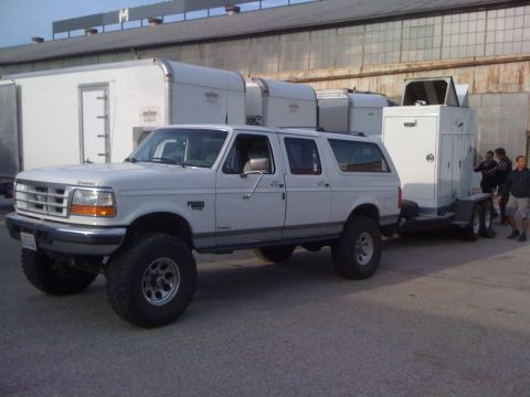 1996 Ford C-350 (Centurion Conversions) - 1996 Ford Bronco SUV is seen towing a trailer with equipment in front of a building.