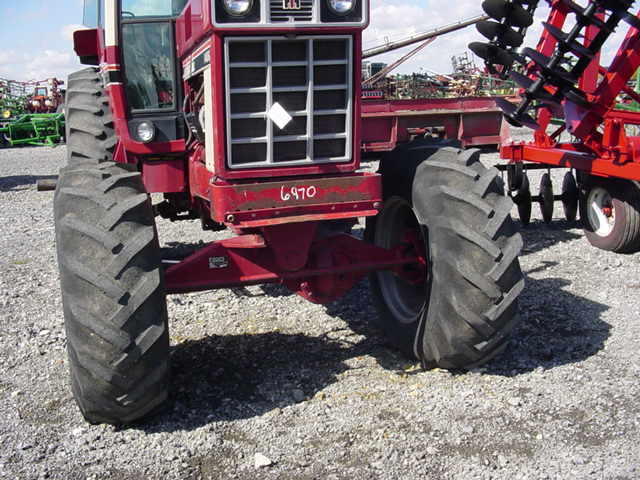Front view of a red tractor with large tires, attached to a red disc harrow. Another red tractor and green equipment are in the background