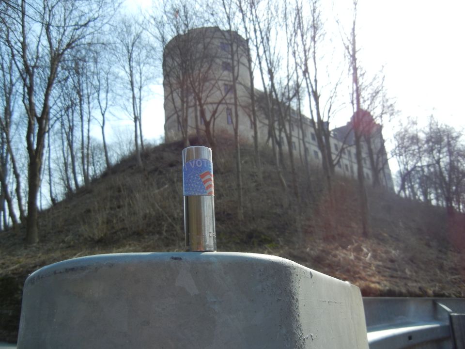 metal pole with a voting sticker on it, in front of a castle on a hill