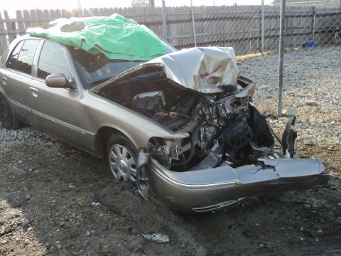 2004 Mercury Grand Marquis - This heavily damaged Mercury Grand Marquis sits in a lot with its front end crushed and covered by a tarp.