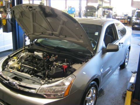 1976 Ford Ranchero - Silver hatchback in a garage with the hood open, revealing the engine. Another vehicle is parked in the background.