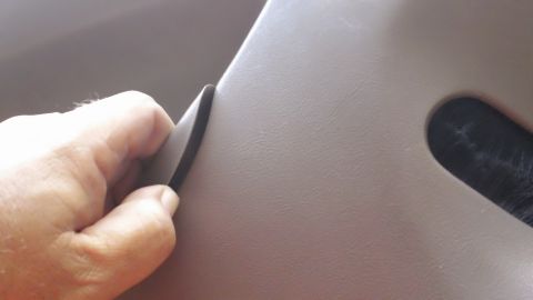 1994 Ford Bronco - Extreme close-up of a hand pinching and lifting a split seam in tan grained vinyl upholstery, revealing the dark gap beneath. A dark slotte…