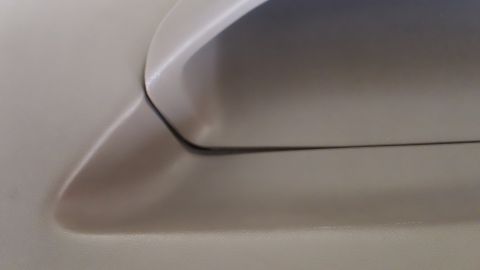 1994 Ford Bronco - Tight close-up of a tan molded interior trim panel where a smooth plastic handle or armrest meets the recessed grip pocket. The panel is cl…