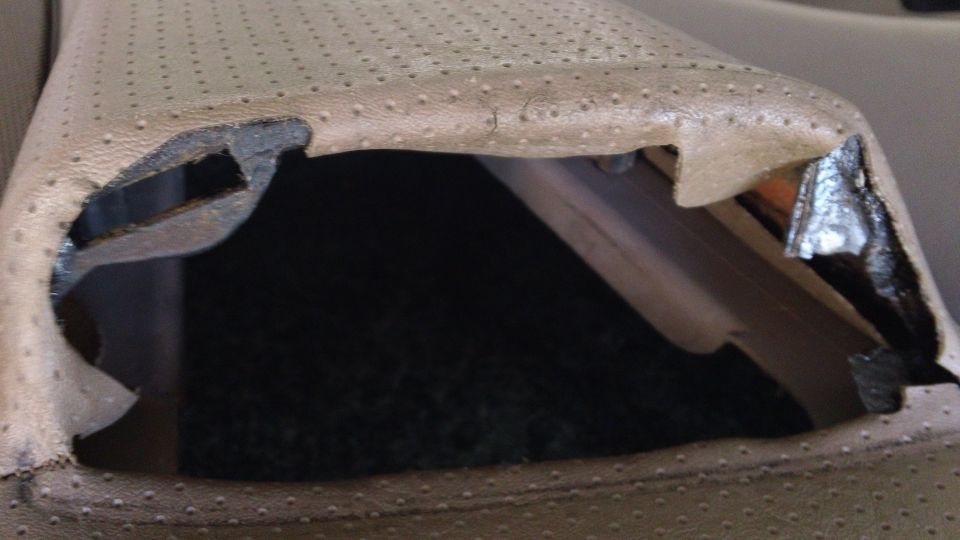 Tan perforated leather seat cushion lifted, exposing black seat frame and carpet