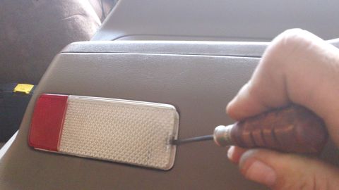 1994 Ford Bronco - A hand uses a screwdriver to remove a reflector from a vehicle's interior panel.