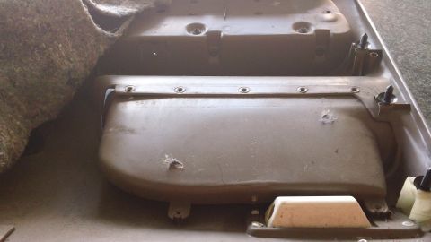 1994 Ford Bronco - A tan molded plastic door panel or interior kick trim lies face-up on a concrete floor, showing a row of screw holes along its top rail, mo…