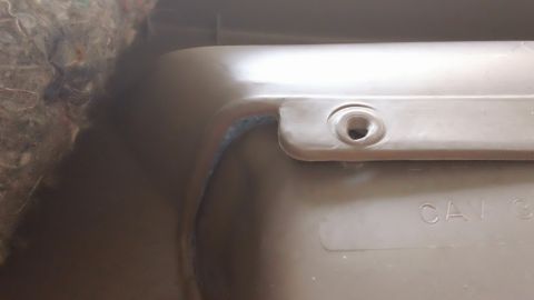 1994 Ford Bronco - Extreme close-up of a tan molded plastic interior trim panel showing a countersunk screw hole and a molded "CAV" marking along its raised e…
