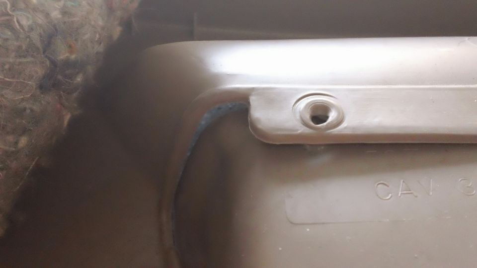 Close-up of tan plastic interior trim panel with screw hole and CAV marking