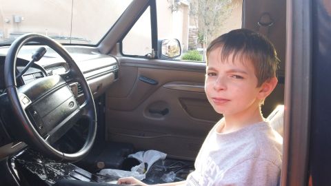 1994 Ford Bronco - A boy in a gray T-shirt sits in the passenger area of a Ford truck cab with the door open, alongside the tan interior with Ford-badged airb…