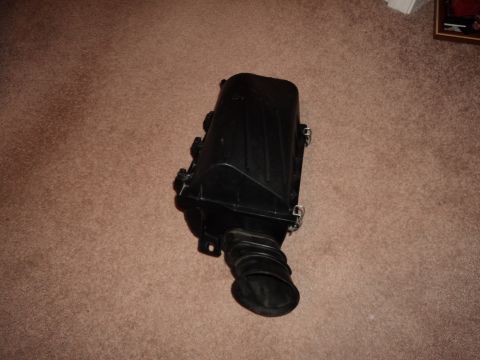 2004 Mercury Grand Marquis - A car part, an air intake box, is shown on a carpeted floor.