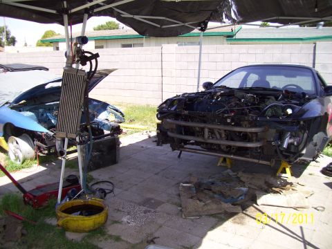 1995 Ford Probe - Two cars are disassembled and worked on under a canopy in a driveway.