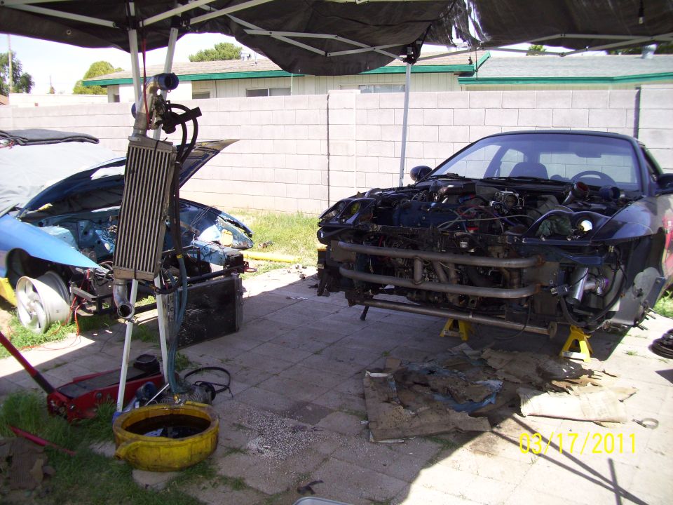 Two cars disassembled under a canopy, one blue and one black, with engines exposed