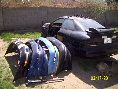 1995 Ford Probe - A black coupe sits with several colorful fenders lined up in front of it, suggesting a project car or parts collection.