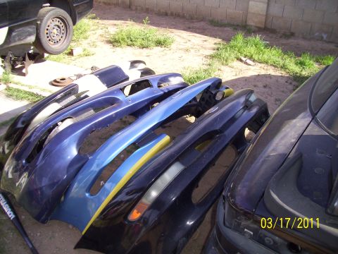 1995 Ford Probe - Multiple car bumpers are piled up outdoors, with a car body visible on the right.