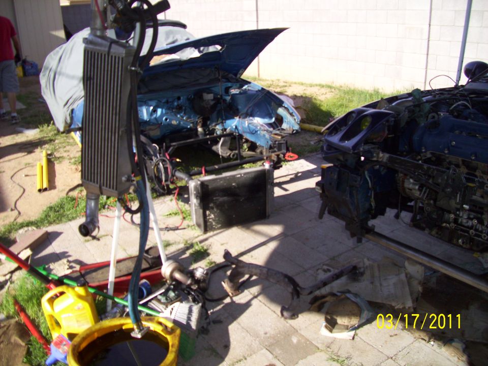 Two disassembled blue cars with hoods open, parts scattered on the ground