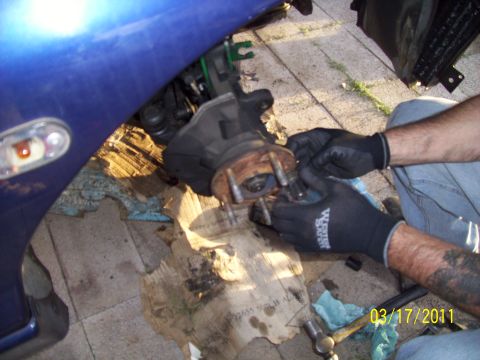 1995 Ford Probe - Hands in black gloves work on a car's front wheel hub assembly, with a blue fender visible.