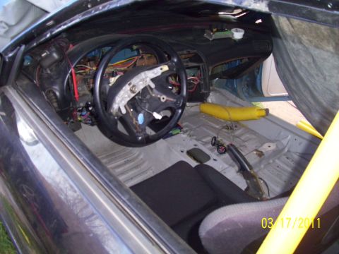 1995 Ford Probe - The interior of a car shows exposed wiring and a disassembled dashboard, with a racing seat visible.