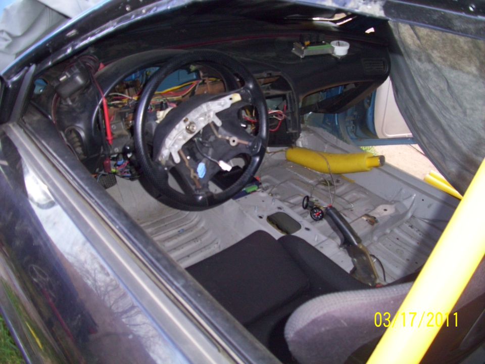 Interior of a car with exposed wiring, removed dashboard, and racing seat