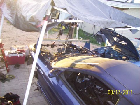1995 Ford Probe - Two cars are visible, one with its interior exposed and engine being worked on under a tarp.