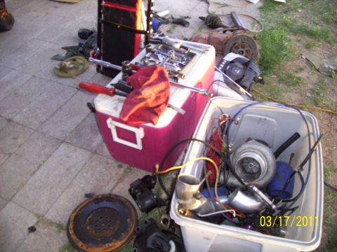 1995 Ford Probe - Various car parts, including a turbocharger, are laid out on the ground next to toolboxes and a cooler.