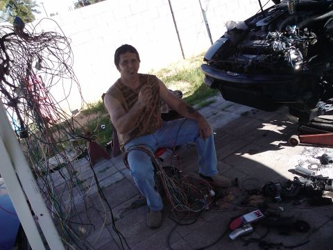 1995 Ford Probe - A man sits amidst a tangle of wires, with the front end of a disassembled car beside him.