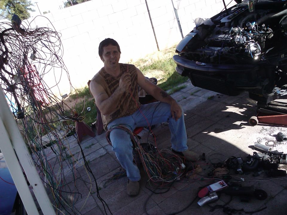 Man sits with car wiring harness next to disassembled car front
