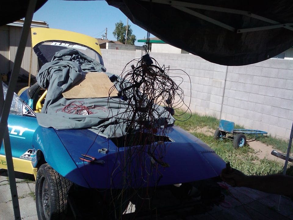 Blue car with yellow hood, covered with tarp and tangled wires. Tools on the trunk