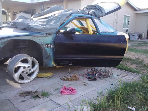 1995 Ford Probe - A partially disassembled car sits outside, with its door ajar and a tangle of wires on the ground.