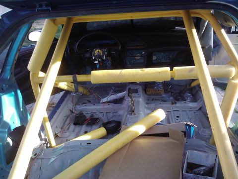 1995 Ford Probe - Car interior stripped down, showing a yellow roll cage and exposed wiring.