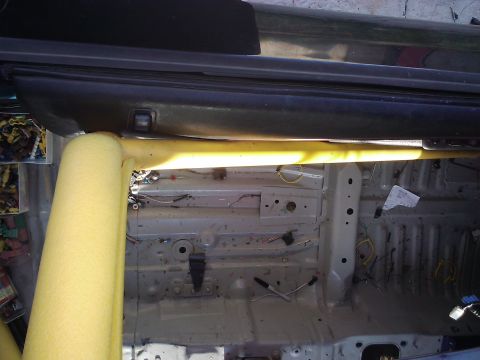 1995 Ford Probe - The interior of a car shows a stripped-down floor and a yellow padded roll cage, suggesting modifications or indicating modifications.