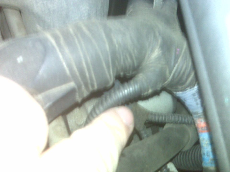 Hand holding a rubber boot in a cramped engine bay