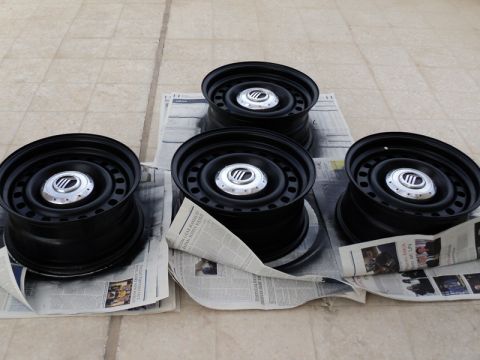 2001 Mercury Grand Marquis - Four black steel wheels with Mercury center caps are laid out on newspapers, likely for painting.
