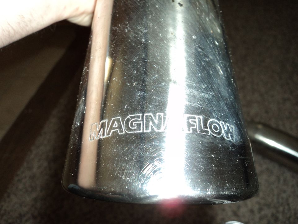 Chrome exhaust tip with 'MAGNAFLOW' logo etched into it, held by a hand