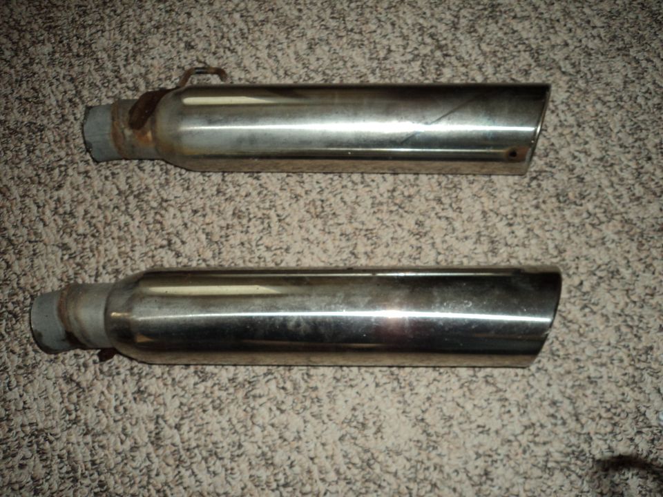 Two chrome exhaust tips on a carpeted surface. One has a rusty clamp