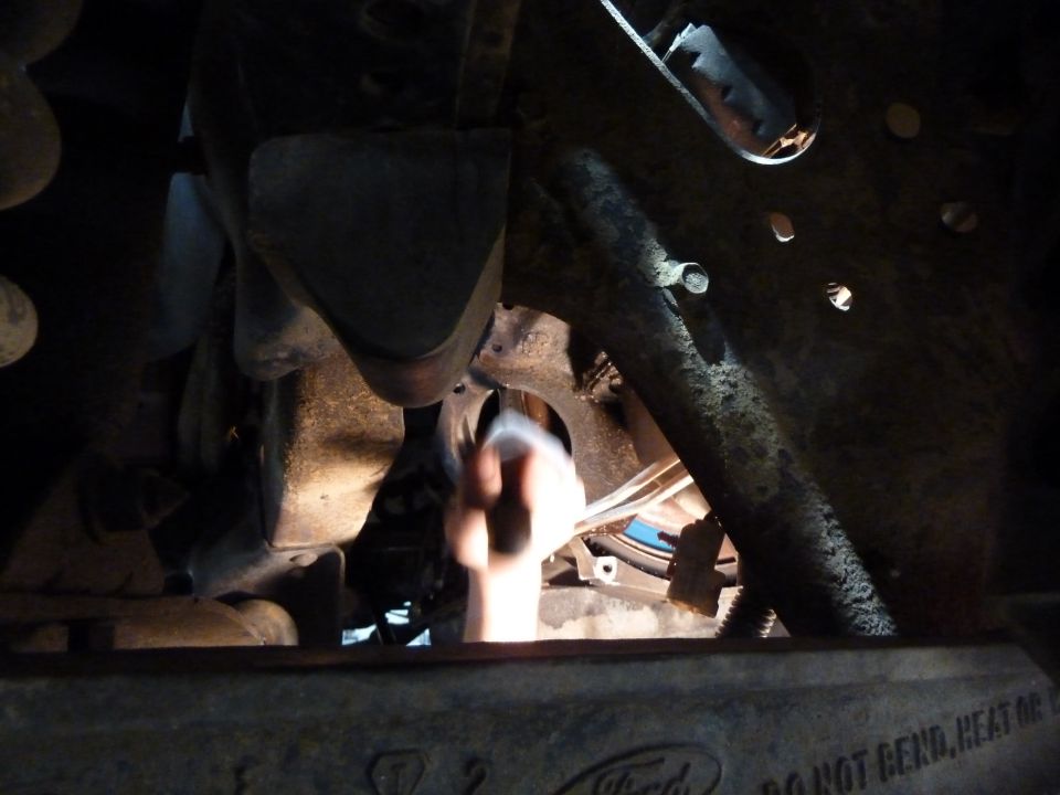 Underbody view of a Ford truck with a hand working on the transmission
