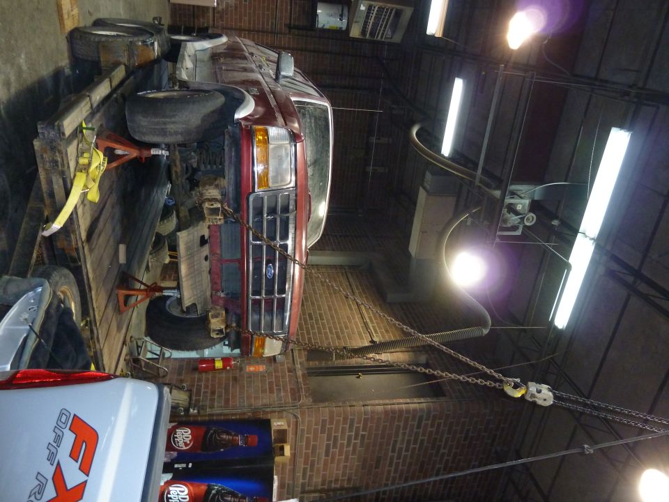 Dark red Ford pickup front end parked in a brick-floored shop with tires and pallets nearby.