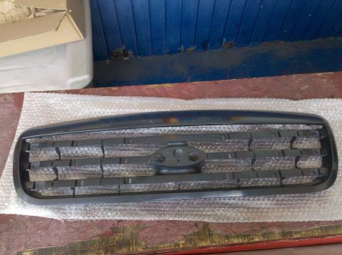 1998 Ford Crown Victoria - dark gray vehicle front grille with a center oval emblem laid on bubble wrap atop a workbench against a blue wall.
