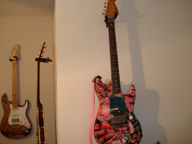 Three electric guitars hanging on a wall, one with colorful floral graphics