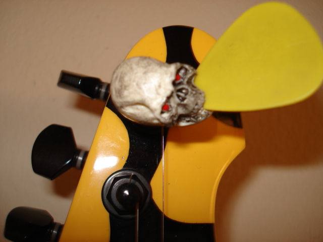 Yellow-and-black electric guitar headstock with skull ornament and yellow pick
