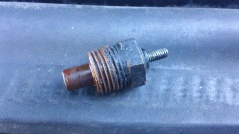 1994 Ford Bronco - A removed single-terminal engine sender unit, likely a coolant temperature or oil pressure sending unit, with rust-stained threads, a hex b…