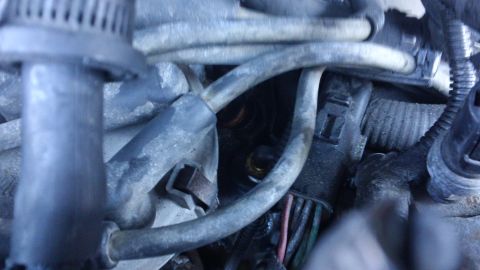1994 Ford Bronco - Grimy engine-bay close-up with spark plug wires and boots crossing over a cast aluminum intake or housing, a black connector with green and…