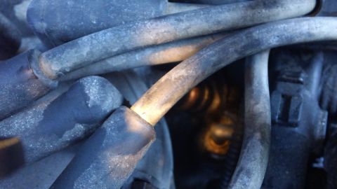 1994 Ford Bronco - Very close view of dusty black spark plug wires with rubber boots routed over engine components, with a rusty coil spring or bracket visibl…