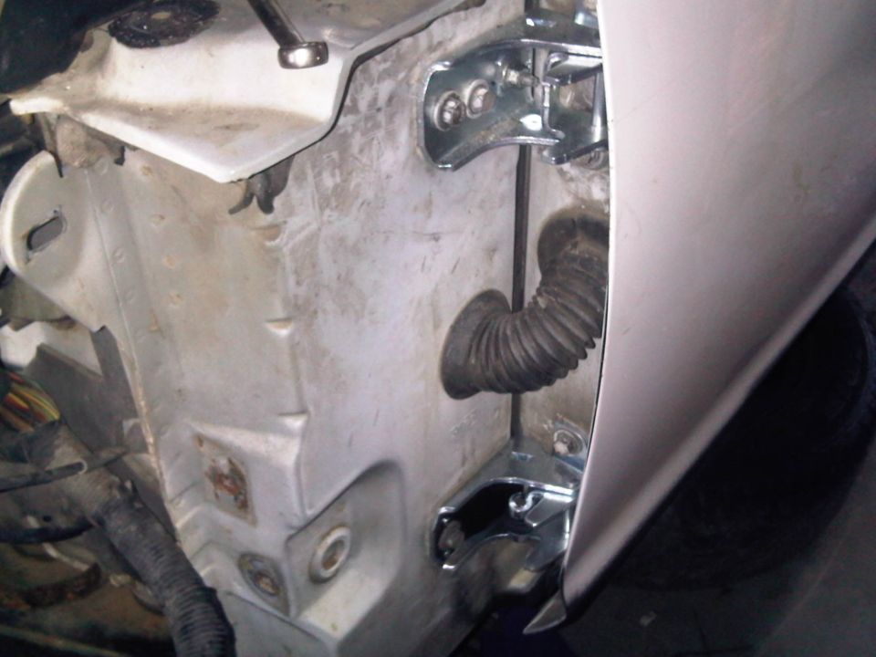 Silver car door hinges and inner body structure exposed with fender removed, black wiring boot visible