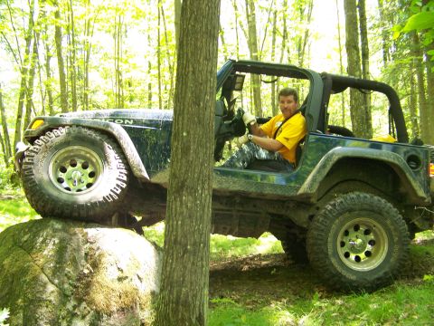 2004 Jeep Wrangler - A dark blue 2004 Jeep Wrangler navigates a rocky trail in a wooded area, with the driver behind the wheel.