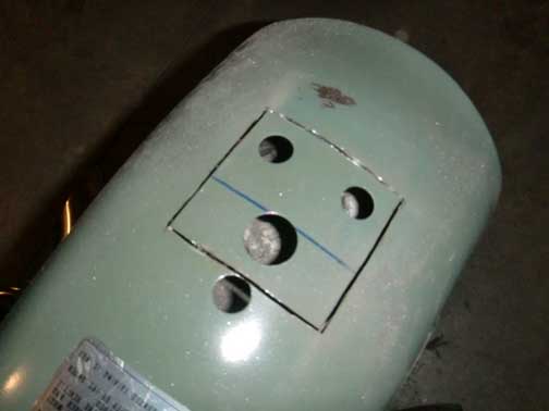 Green cylindrical tank with a square cutout and three circular holes. A label is visible on the lower left